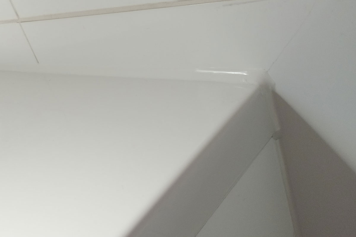 Kitvoeg in de hoek van een badkamer, strak en wit afgewerkt