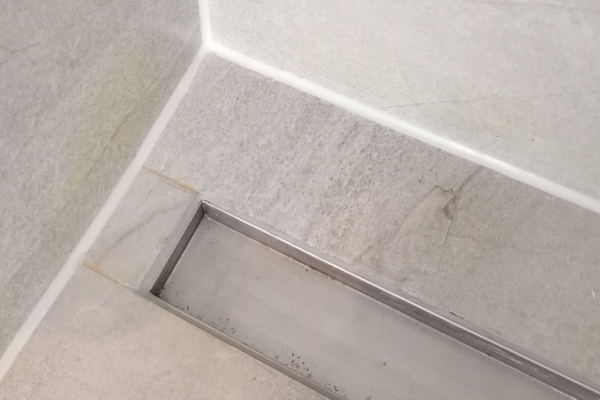 Douchegoot met nieuwe witte kit in een betegelde douchevloer