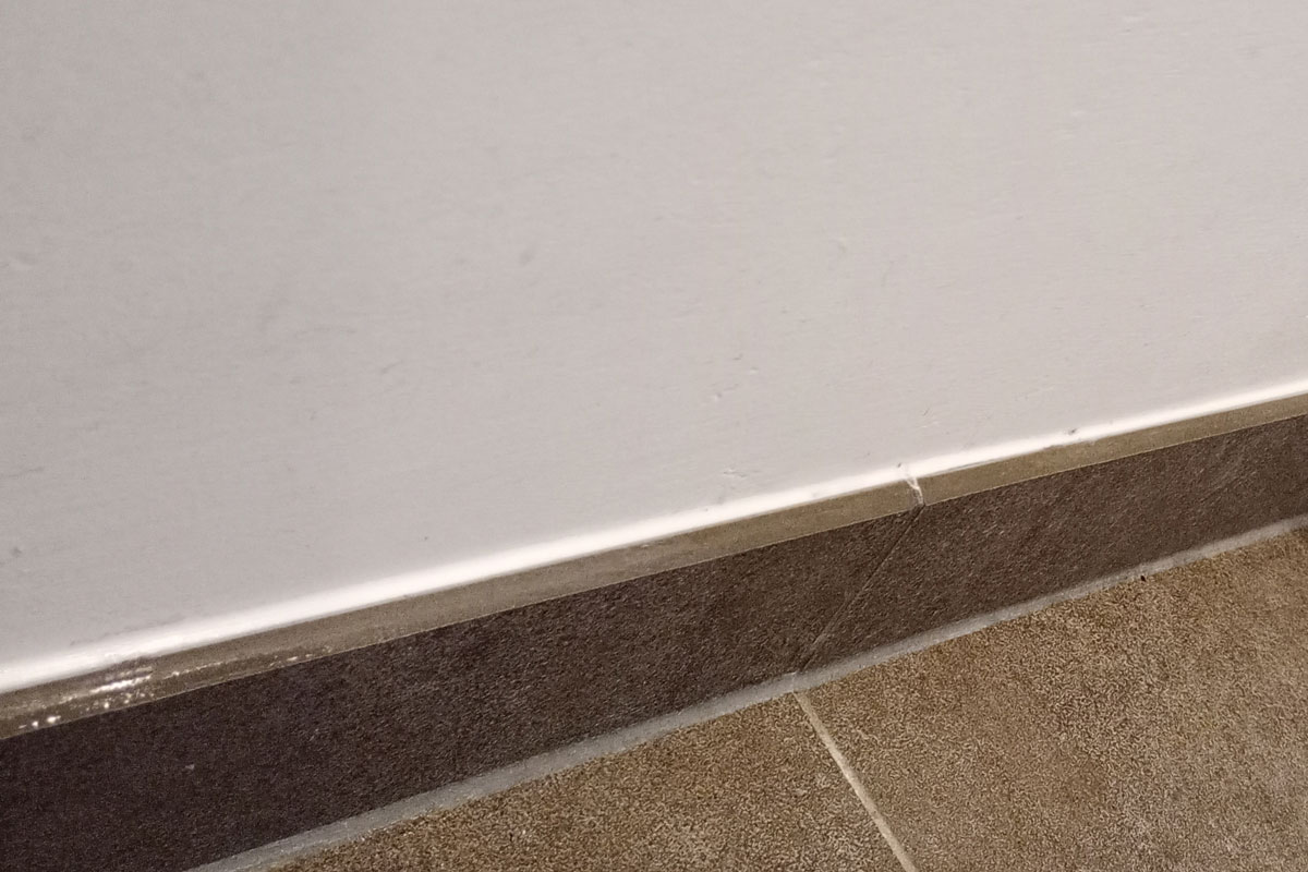 Tegelplint met een kitnaad aan de bovenkant tegen de witte wand en aan de onderkant tegen de tegelvloer