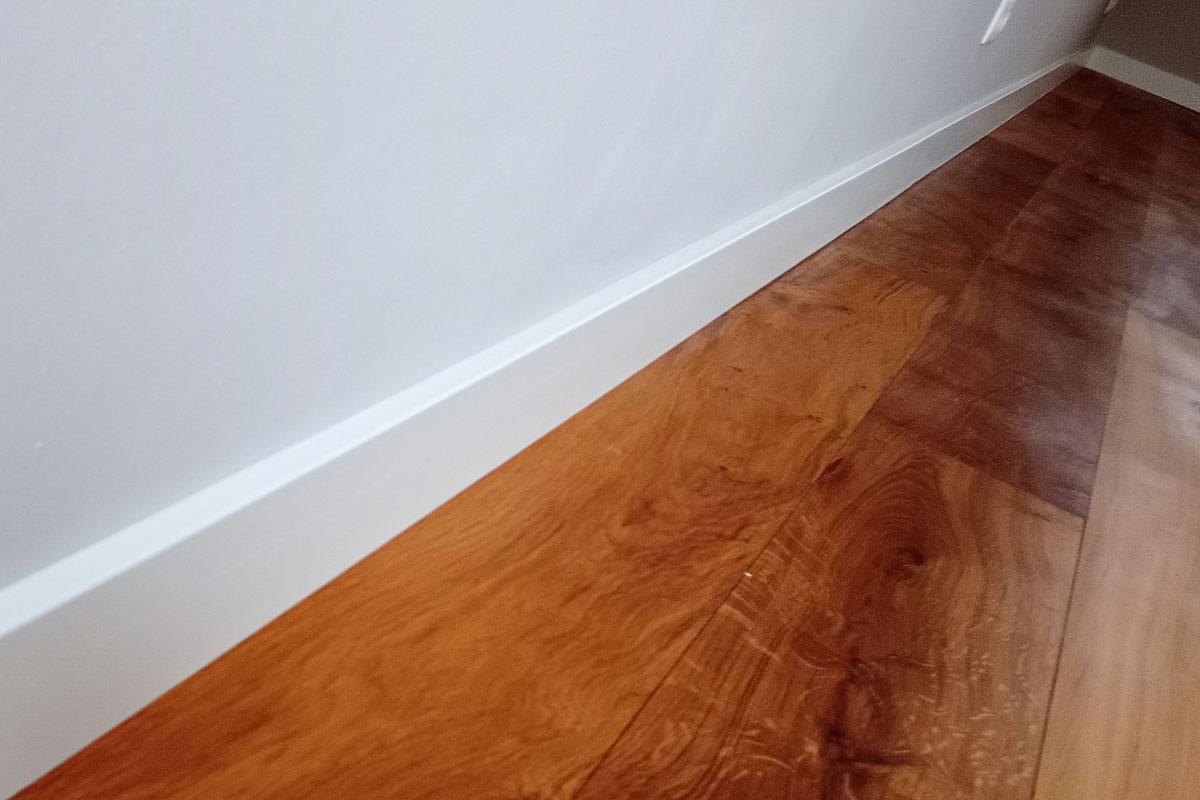 Kitwerk bij een witte plint: strakke kitvoeg tussen plint en wand, naast een houten vloer