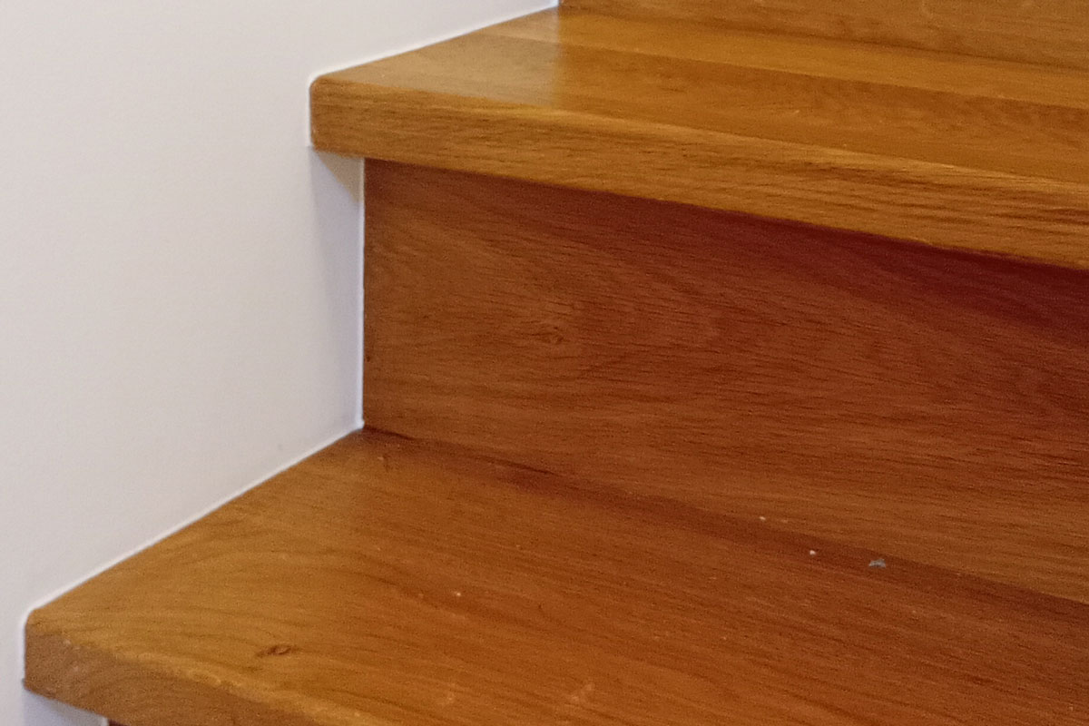 Detail van de kitrand tussen een eiken trede en de witte wand